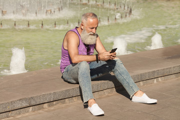 Trendy senior man using smartphone in downtown center outdoor - Mature fashion male having fun with new trends technology - Tech and joyful elderly lifestyle concept