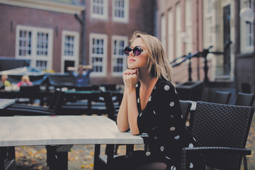 Fototapeta premium Young girl in black dress and sunglasses in Amsterdam cafe. Holland, Netherlands