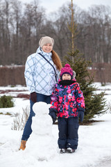 Fototapeta na wymiar Full length portrait of mother, child and snowman, people play with snow in winter park