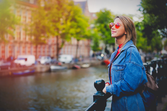 Young girl in red sweater and orange sunglasses with backpack at bridge in Amsterdam street. Holland, Netherlands. Autumn season