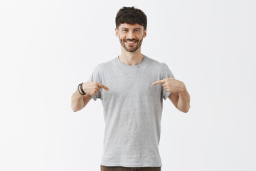 Man being proud of personal achievements. Portrait of good-looking friendly and confident happy guy with beard and stylish hairstyle pointing at himself with index fingers and smiling