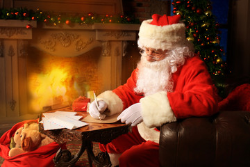 Portrait of happy Santa Claus sitting at his room at home near Christmas tree and answering Christmas letters.