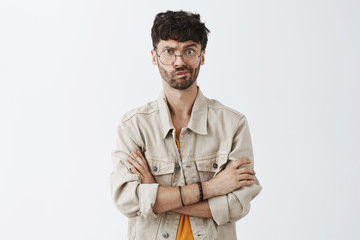 Waist-up shot of intense dissatisfied handsome mature caucasian guy with beard in beige jacket holding hands crossed on chest smirking and frowning facing trouble on work thinking and doubting