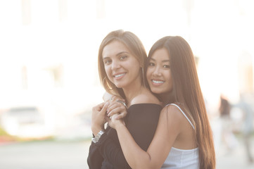 Two young women hugging outdoors. Asian girl looking at the camera and smiling. Best friends