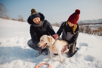 Friendship with the dog. Couple playing in the winter in the snow with a labrador dog in the park.
