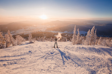 Young woman on snowboard raised her hands up, joy to sunrise. Sheregesh Ski Resort