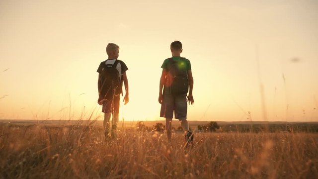Two travelers boy. Two boys are walking along the field at sunset with rucksacks. The concept of family and travel
