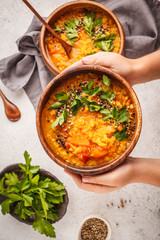 Yellow Indian vegan lentil soup curry with parsley and sesame in a wooden bowl in hands.