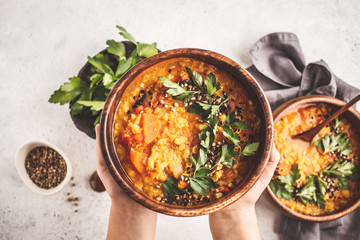 Yellow Indian vegan lentil soup curry with parsley and sesame in a wooden bowl in hands. - obrazy, fototapety, plakaty