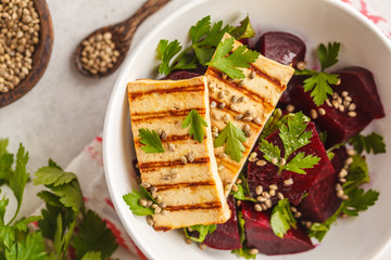 Baked beet salad with grilled tofu parsley and oil in a white bowl, top view.