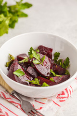 Baked beet salad with parsley and oil in a white bowl.