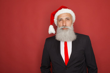 Pensive man look in camera. Styling old man with a long white beard posing on the red background in modern strict suit. Portrait of modern Santa Claus.