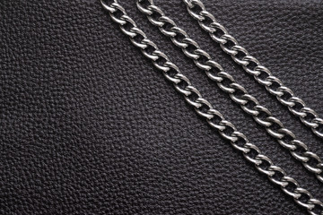 Metal silver chains on luxury black leather texture.
