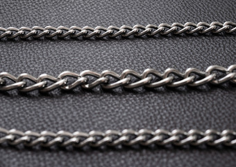 Metal silver chains on luxury black leather texture.