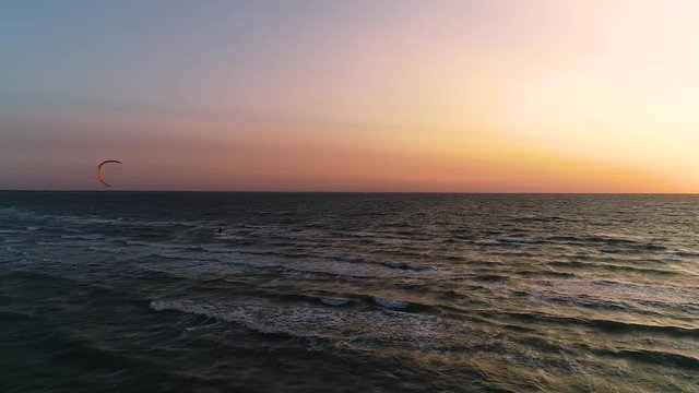 Sunset at sea, kitesurfer riding on waves. Aerial view