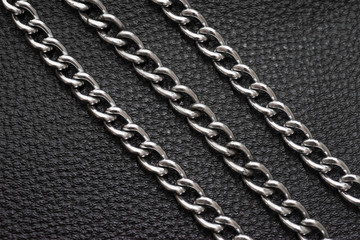 Metal silver chains on luxury black leather texture.