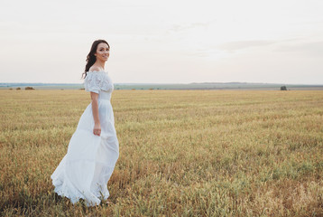 Fototapeta na wymiar Beautiful young woman in the white dress on the field