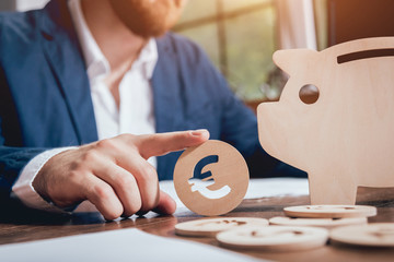 Businessman holds a coin near wooden piggy. Money box. Collecting money with earning bank.