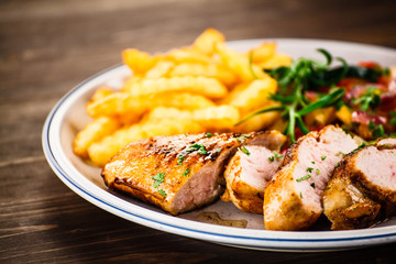 Grilled chicken fillet with french fries on wooden background