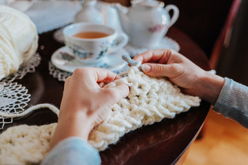 Woman's hands crocheting with white wool on the kitchen table