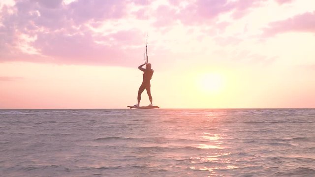 A kitesurfer man does the trick in the air and lands in shallow water, slow motion