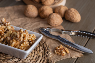 Walnuts in a white bowl and a nutcracker on the wooden table
