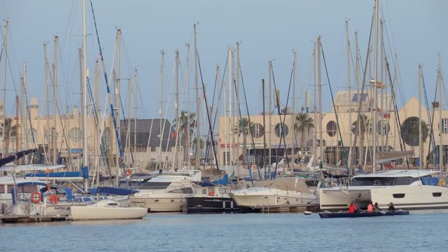 ALICANTE, SPAIN - APRIL 19, 2018: Harbour scene with yachts mooring and rowing boat with women sailing by