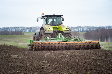A tractor pulls a disc harrow system implement to smooth over a dirt field in preparation for...