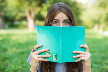 Beautiful girl covering her face with book. Education and people concept.