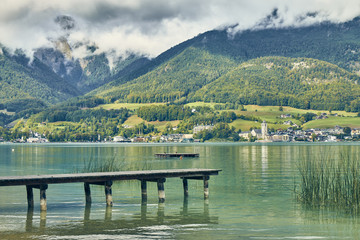 Landscape view of cyan colored Wolfgangsee lake with a deck from Gschwendt village coast in Austria.