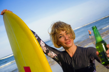 Obraz premium young sexy beautiful and happy surfer woman holding yellow surf board smiling cheerful drinking beer bottle enjoying summer holidays in tropical beach