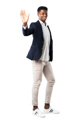 Full body of Handsome african american man wearing a jacket saluting with hand with happy expression on white background