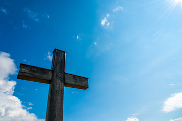 Simple oak wood catholic  cross, visible sunlight perfect blue sky with white clouds.