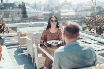 Calm lady telling with man while eating and gesticulating hand. She sitting at table with him...