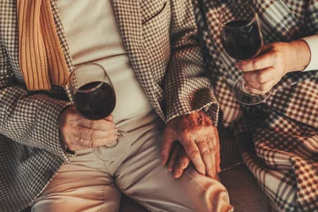 Cercles muraux Bar Top view of wrinkled female and male hands holding glasses with wine. Couple sitting on couch