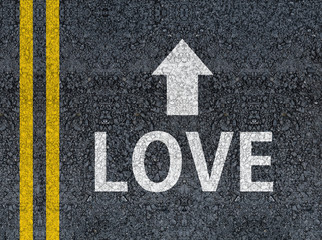 Word LOVE with arrow written with paint on road asphalt