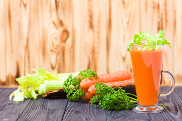 Carrot and celery juice with fresh vegetables on bark plates on wooden background.