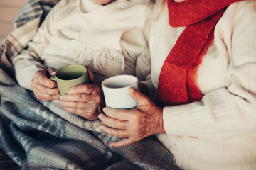 Close up of cup for beverage in male and female palms of mature couple, covered with plaid