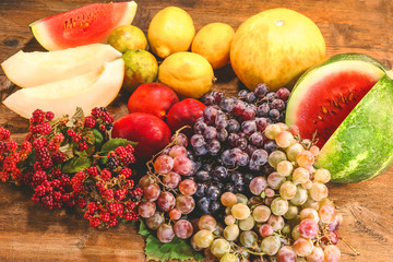 various summer and autumn fruits. watermelon. melon, peaches and grapes. lemon and lime. on a wooden table.