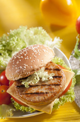 Chicken burger with bell pepper and lettuce with cherry red and yellow tomato on yellow background 