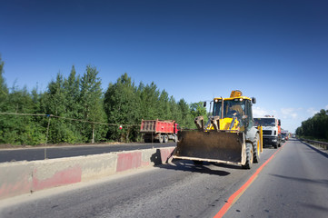 Tractor rides on the asphalt road with red and white safety concrete blocks