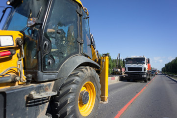 Tractor rides on the asphalt road with red and white safety concrete blocks