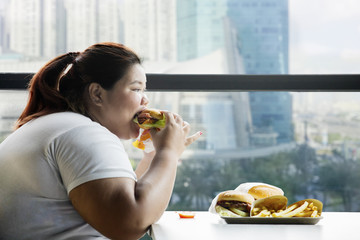 Fat woman eating a hamburger in the restaurant