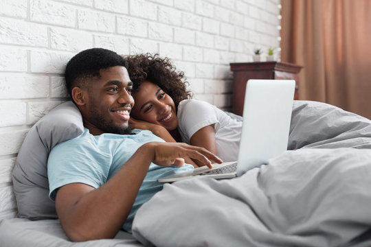 Happy black couple in bed with laptop at home