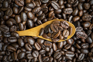 Heap of roasted coffee beans with wooden spoon
