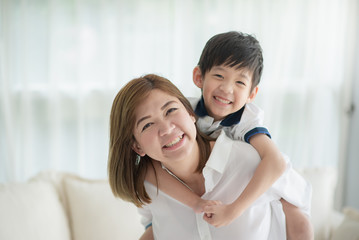 Asian child on a piggy back ride with his mother at home