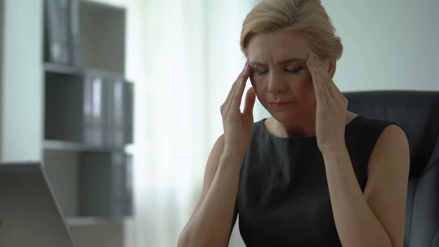 Tired female boss sitting at office table, suffering from headache and tension