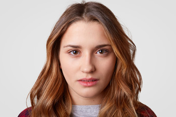 Fototapeta premium Close up shot of beautiful European woman with self confident expression, looks directly at camera, has healthy skin, wavy dark hair, listens something attentively, isolated over white background