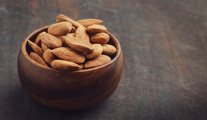 Almonds in a wooden bowl against dark rustic wooden background with copy space for your text. Horizontal. Overhead view. Vintage effect.