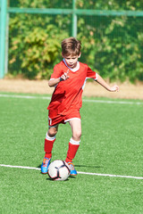 Boy soccer player with ball on football field